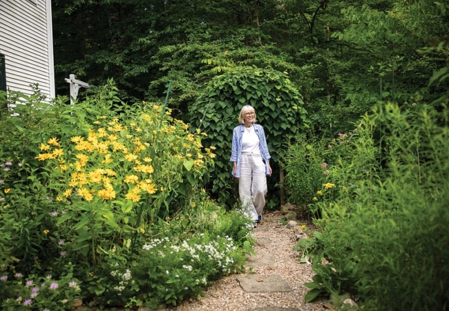 A women walking on a gravel path between tall native flowers and other plants.