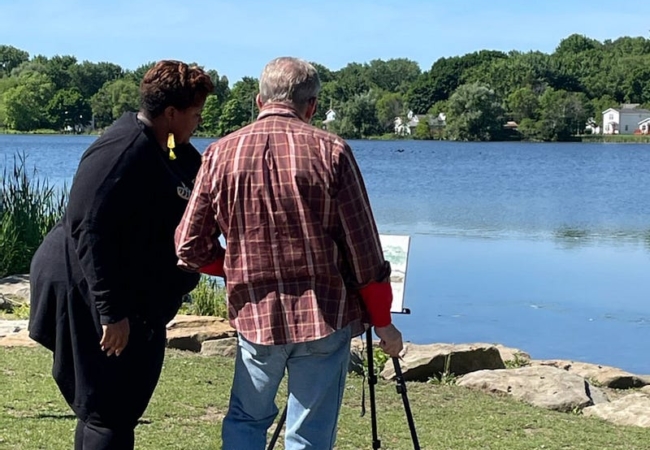 A man and woman stand at an art easel with Summit Lake in the background.