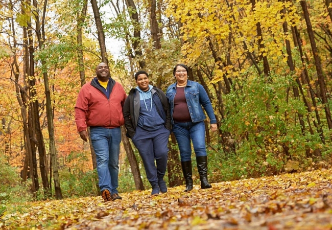 A family of three, a mom, dad and son, walking along a trail during autumn.