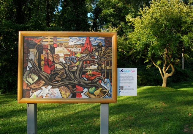 A painting displayed outdoors with an Inside Out plaque attached to its side.