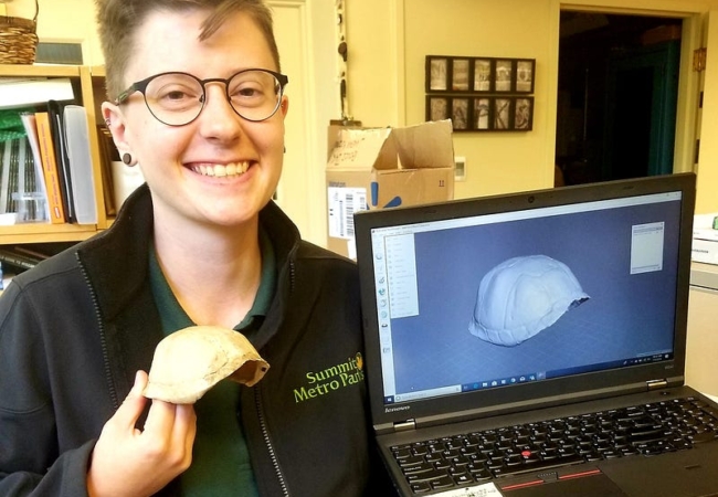 A Metro Parks employee holds a 3D printed turtle shell in one hand and a laptop with a rendering of the shell on screen in the other.