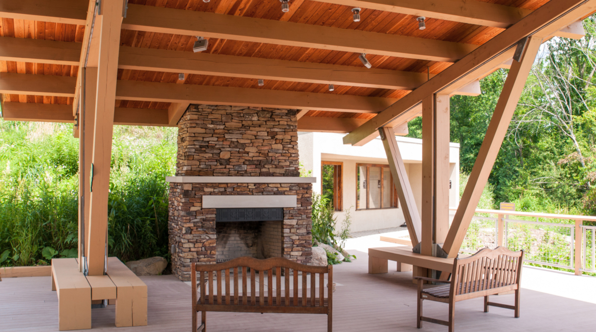 A stone fireplace and wooden benches sit on a covered deck.