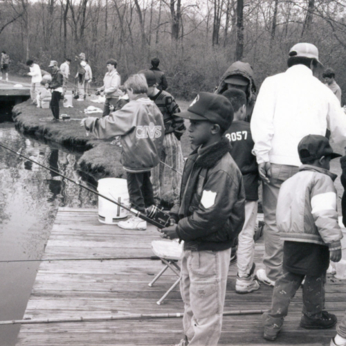 A boy fishing off of a crowded wooden deck.