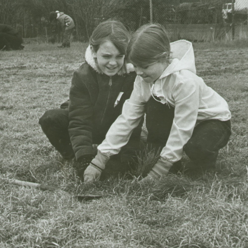 A black and white photo of two girls, whose hands are in the dirt.