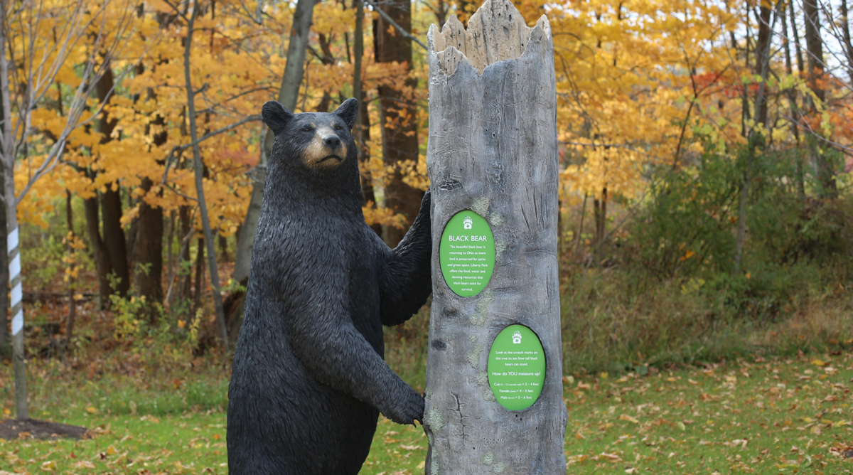 A statue of a black bear leaning against a tall tree stump.