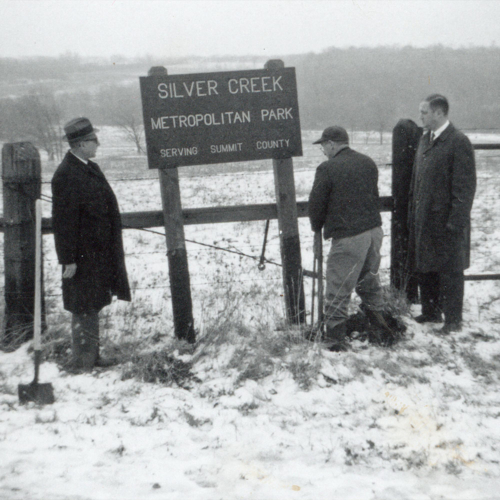 A black and white photo of several men around a wooden sign that reads, "Silver Creek Metropolitan Park, serving Summit County."