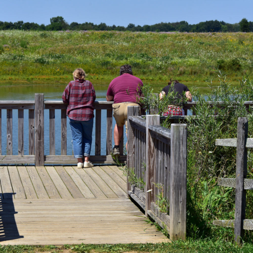 Three people lean against the railing of a small wooden platform.