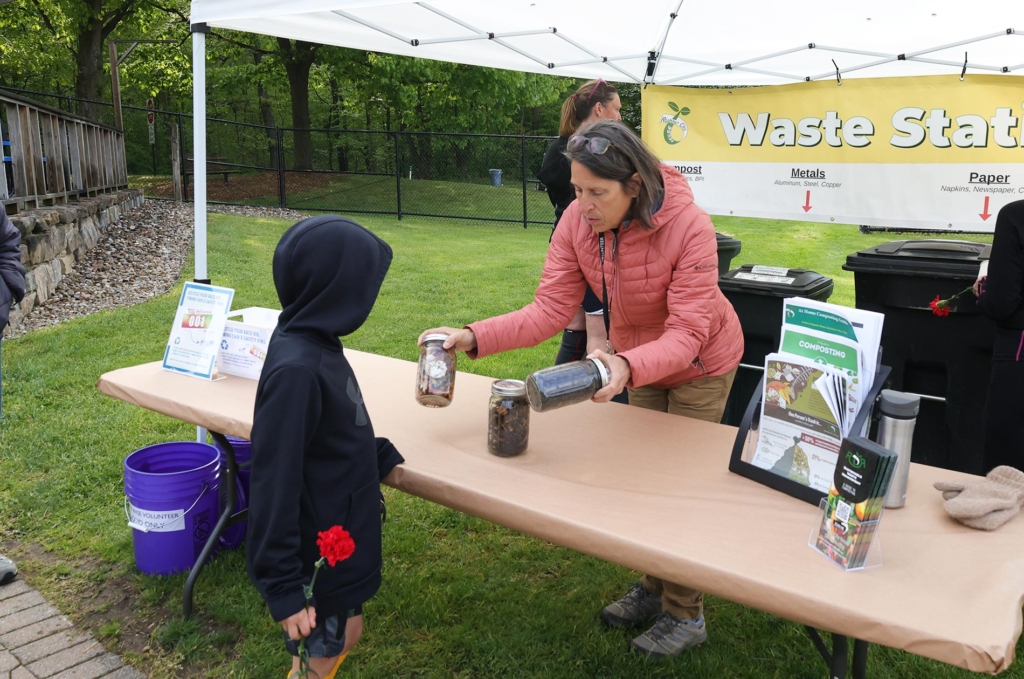 A woman holds two jars up for an interested child. One is filled with food scraps and the other with compost.